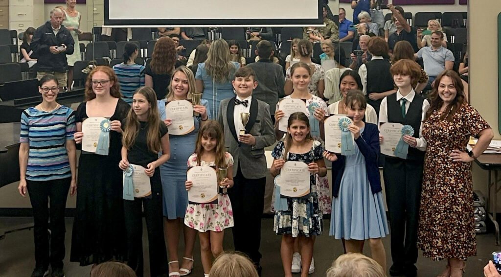 Young musician proudly holding awards after placing as a finalist in the first FLAME Young Musicians Competition